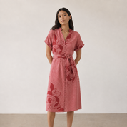 Woman wearing a batik pink dress with floral patterns on a plain background