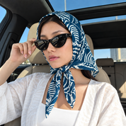 A woman in a car wearing a blue and white ikat patterned headscarf, black sunglasses, and a white top.