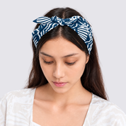 A woman wearing a navy blue and white patterned fabric headband with a bow, looking down against a light gray background.