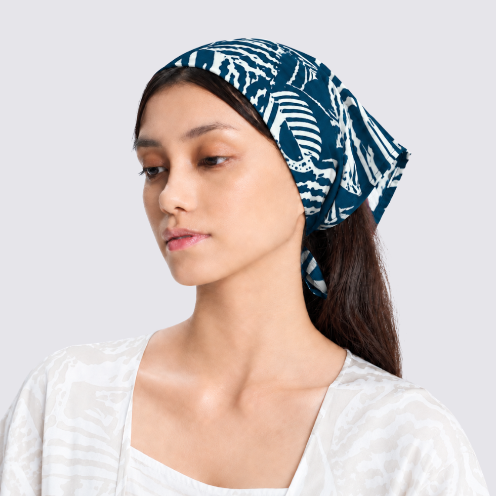 A woman wearing a navy blue and white patterned headscarf, shown from the chest up against a light gray studio background.