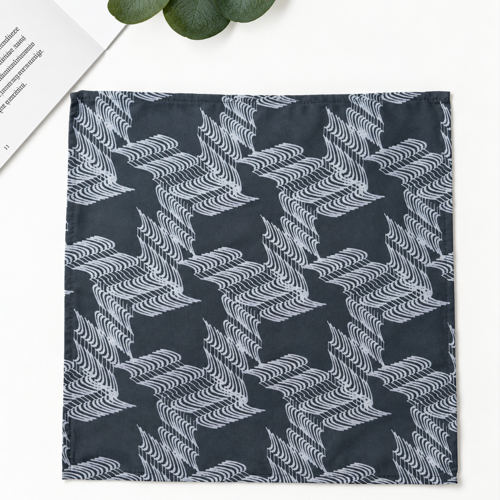 A square fabric item, likely a pocket square or scarf, featuring a repeating houndstooth-like pattern of stylized white birds on a dark charcoal gray background. The item is displayed flat on a white surface with decorative props, including a book corner and green leaves.