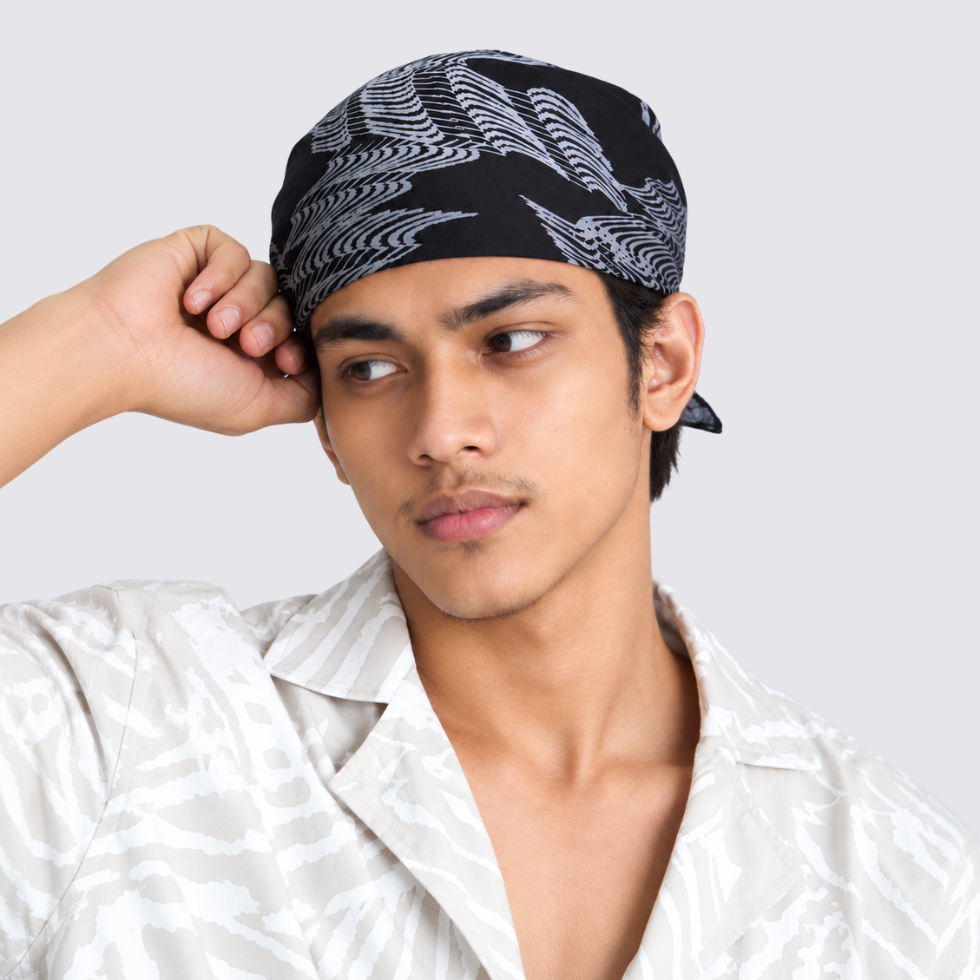 A man wearing a black bandana with a white leaf pattern, paired with a matching light-colored patterned shirt, set against a plain light gray background.