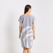 Woman wearing a gray dress with white abstract pattern on a plain background