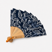 A traditional folding hand fan with a natural bamboo frame, orange handle, and navy blue fabric decorated with a white ikat pattern, shown on a clean white background.