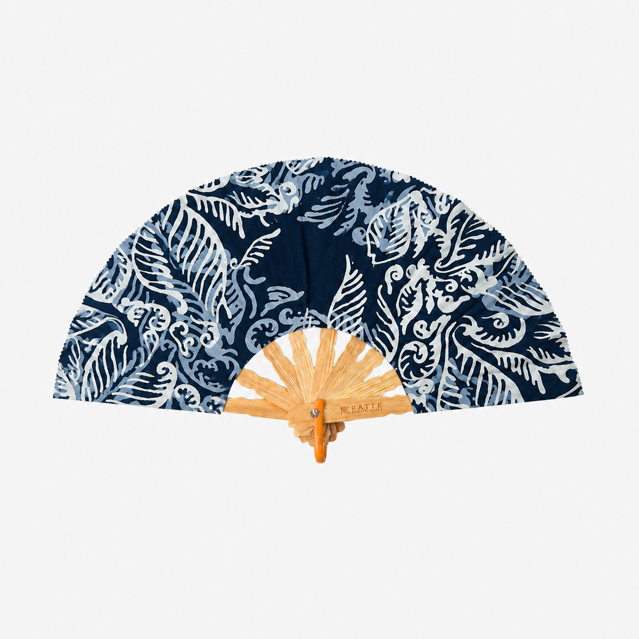 A folding hand fan with a navy blue and white batik pattern on the fabric, featuring a light wood bamboo frame and a small metal brand plaque that reads 'M. LATTIE'.