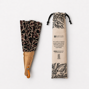 A folded hand fan with a brown and beige batik pattern and a light wood handle, shown next to its beige drawstring pouch with black batik-style illustrations and text.