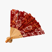 A folding hand fan with a red batik patterned fabric and a natural bamboo handle, shown on a plain white background.