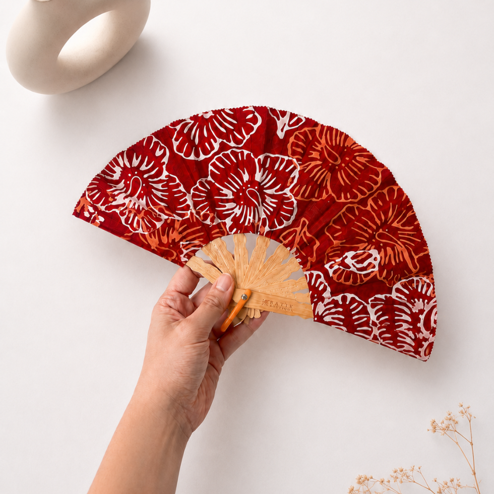 A folding hand fan with a red fabric canopy featuring a white and orange floral pattern, supported by a light wood frame. with a pot and a plant by the backgriund
