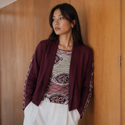 Woman wearing a maroon jacket over a patterned top against a wooden wall.