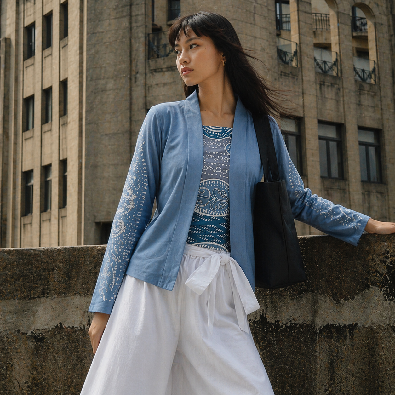 Woman in a blue cardigan and white skirt standing against an urban background