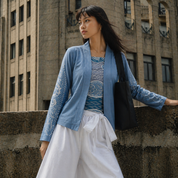 Woman in a blue cardigan and white skirt standing against an urban background