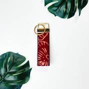 Keychain with red pattern and gold ring on a white background with green leaves