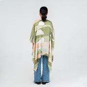 Person wearing a green and pink patterned poncho on a white background
