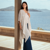 Woman wearing gray printed batik kimono, posing at a wooden viewpoint by the beach