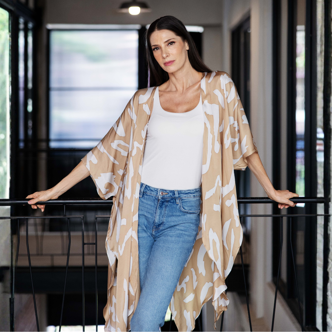 Woman wearing a beige patterned kimono over a white top and blue jeans indoors.