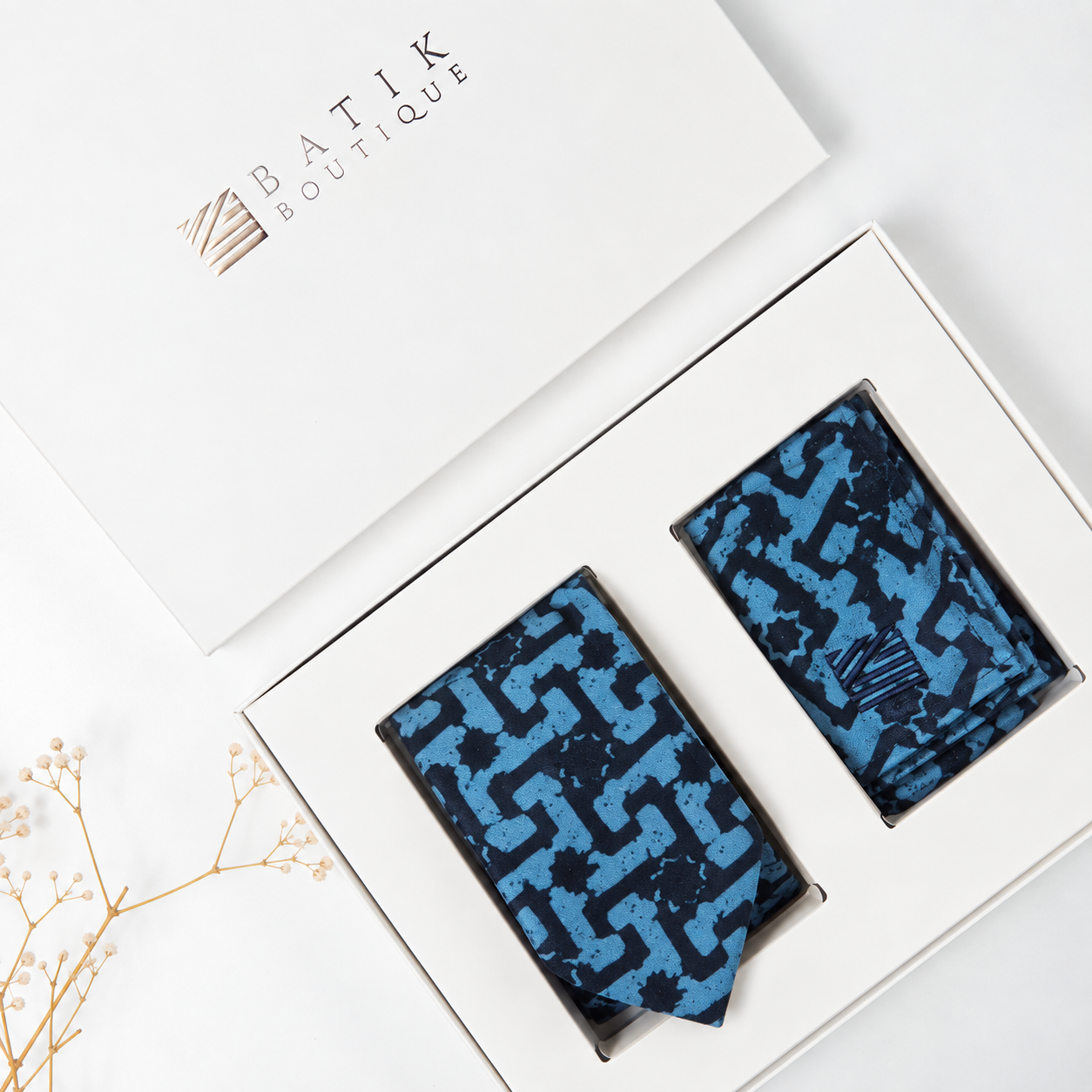 Two patterned neckties in a white gift box with the brand name 'BATIK BOUTIQUE' printed on the lid. The ties have a blue and black geometric maze-like pattern.