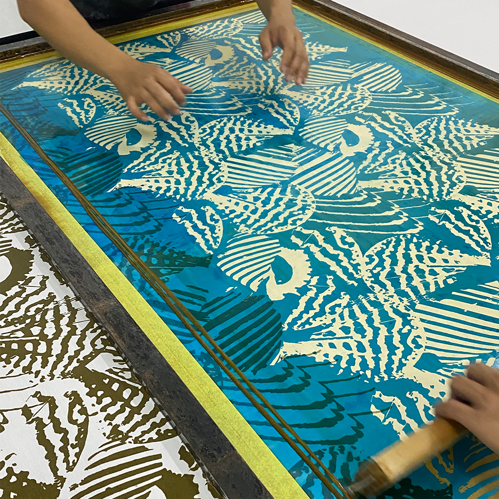 Person using a screen printing technique with a blue and yellow pattern on a wooden screen.