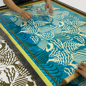 Person using a screen printing technique with a blue and yellow pattern on a wooden screen.