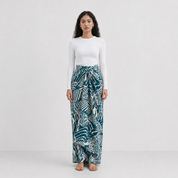 Woman wearing a white top and teal patterned pants on a white background