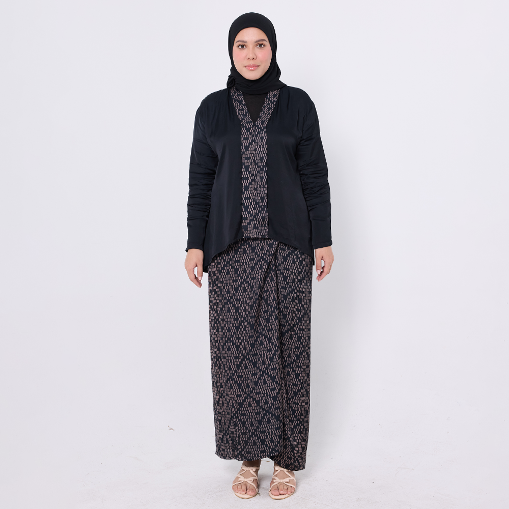 Woman wearing a black outfit with a patterned top and long skirt on a white background