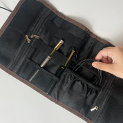 Black knitting needle case with gold needles and a hand reaching in to adjust cables.