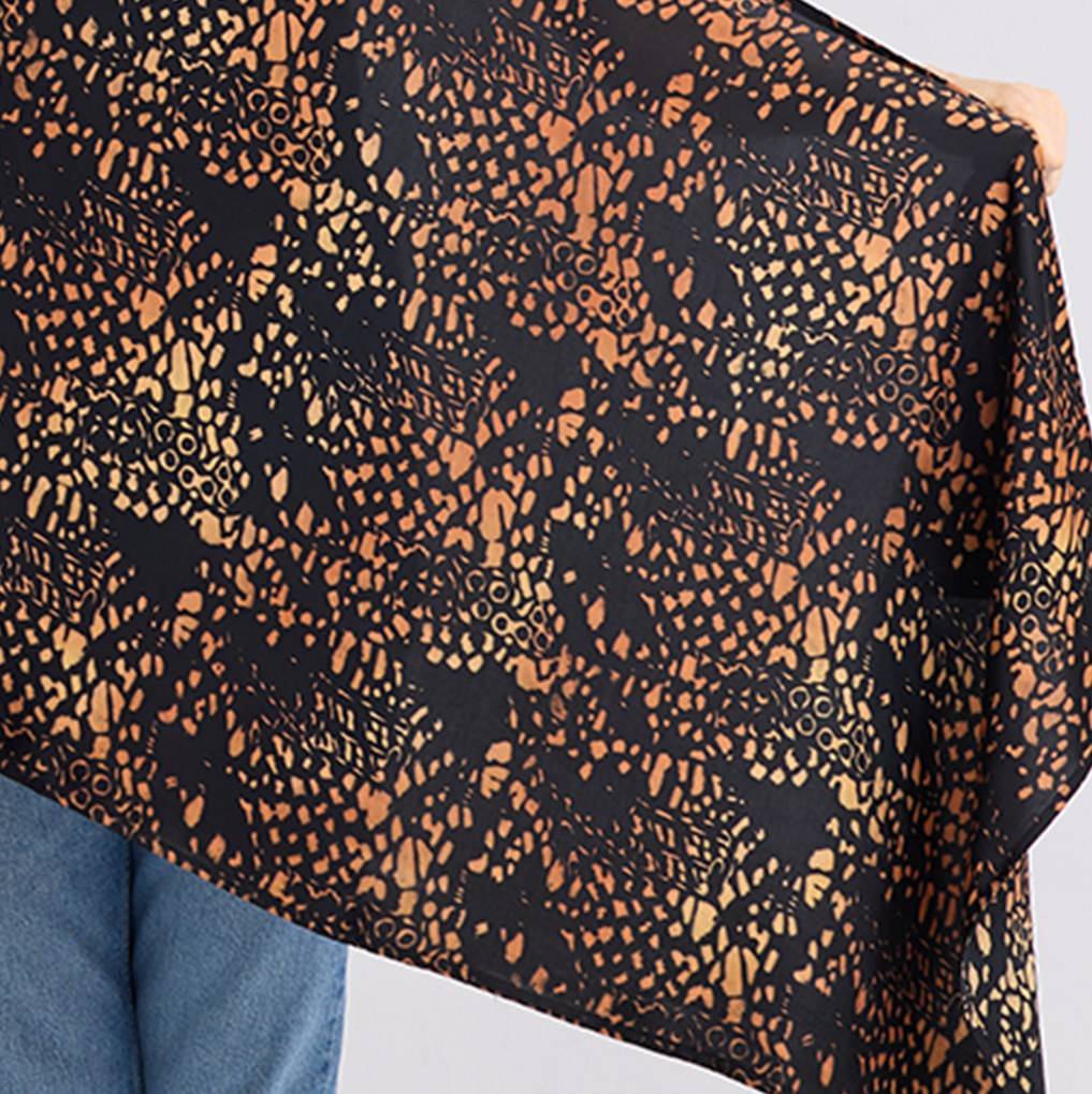 Close-up of a black fabric with orange geometric pattern held by a person wearing blue jeans.