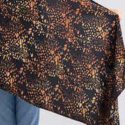Close-up of a black fabric with orange geometric pattern held by a person wearing blue jeans.