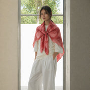 Woman wearing a pink scarf standing in a bright room with large windows.
