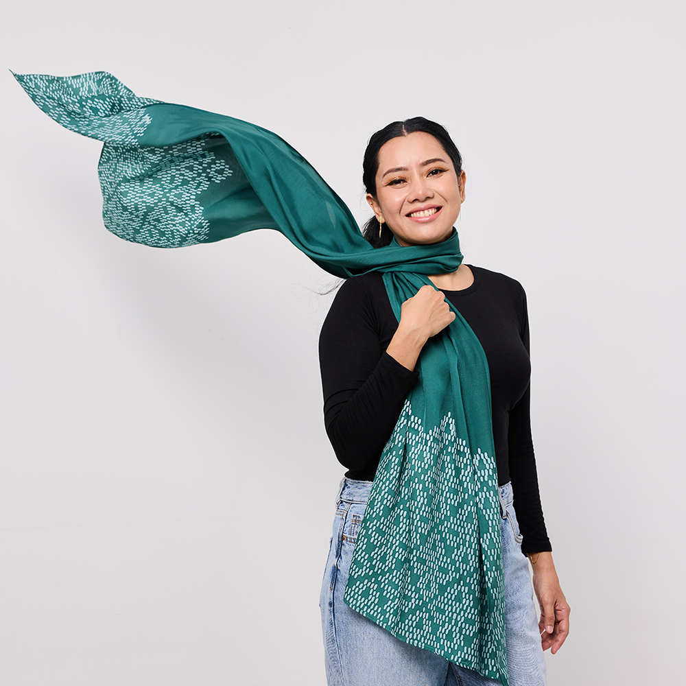 Woman wearing a green scarf with a white pattern against a plain background