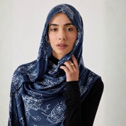 Woman wearing a blue patterned hijab against a plain background