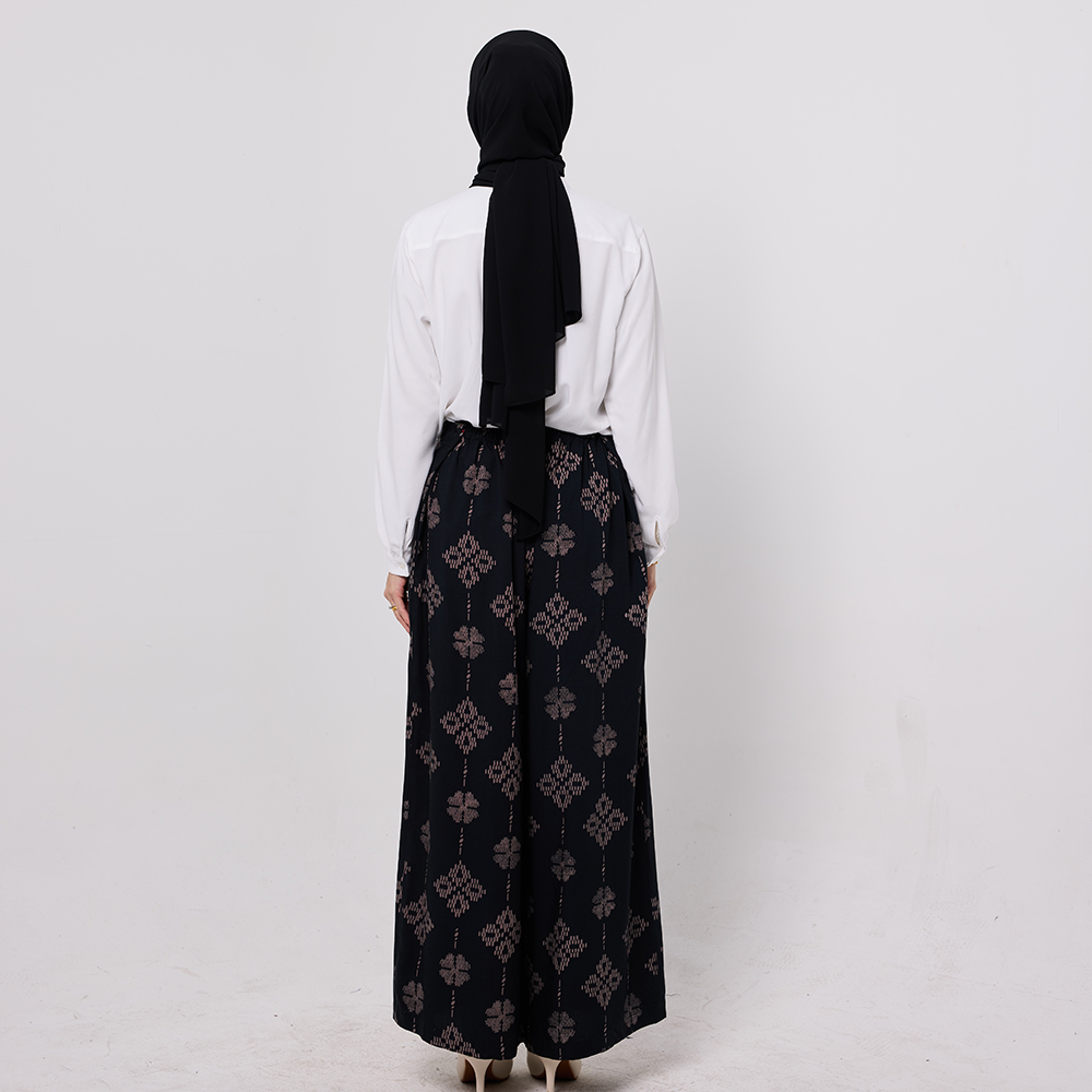 Person wearing a black patterned abaya and white blouse on a light gray background