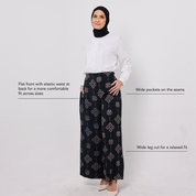 Woman wearing a white blouse and black patterned pants on a light gray background