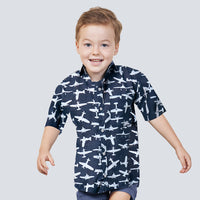 a boy standing in front of white wall wearing batik shirt in black airplane pattern