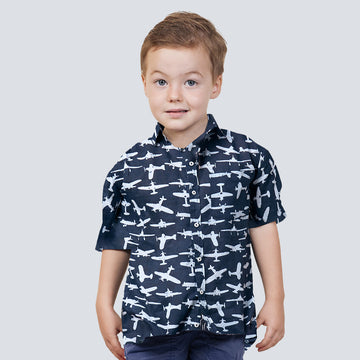 a boy standing in front of white wall wearing batik shirt in black airplane pattern