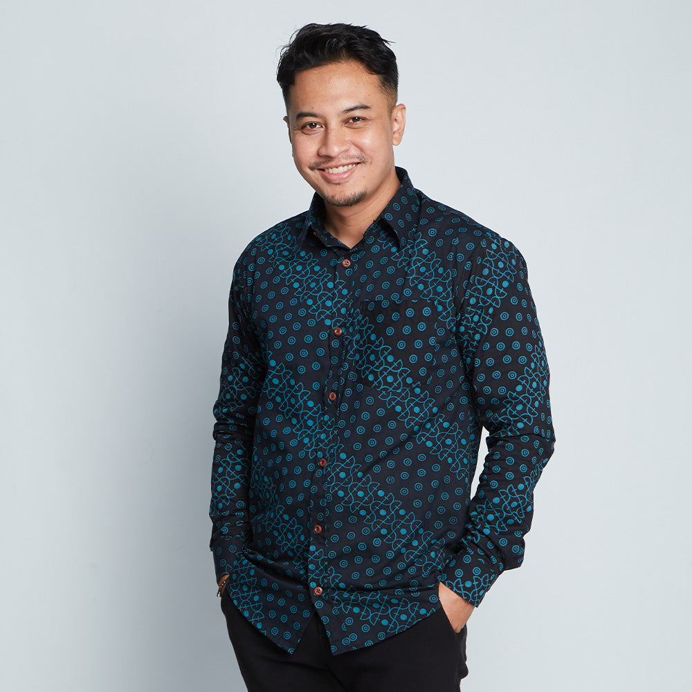 a man standing in front of a white wall wearing a batik shirt in black alur