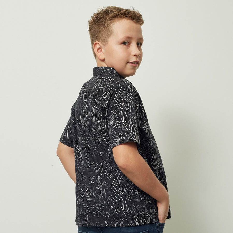 a boy posing in front of a white wall in a black driftwood patterned batik shirt