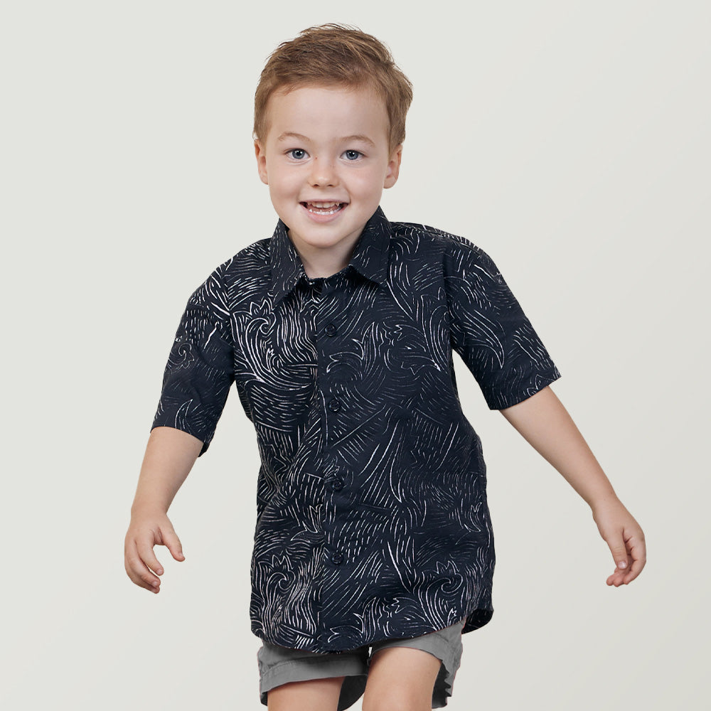 a boy jumping in front of a white wall in a black driftwood batik shirt