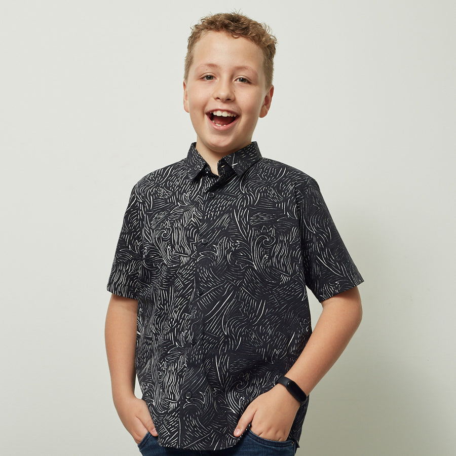 boy standing in front of a white wall in a batik shirt with black driftwood pattern