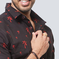 a close-up of a man in front of a white wall smiling as he's posing while wearing a batik shirt in black palm pattern