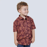 A young boy confidently modeling a Maroon Coral patterned batik shirt against a neutral background