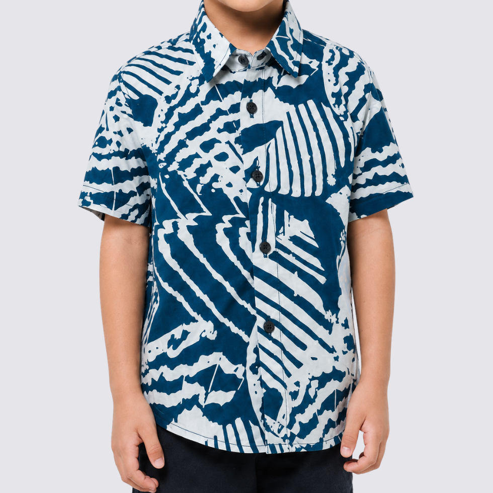 A child wearing a short-sleeve button-up shirt with a bold blue and white abstract zebra-like pattern, photographed against a light gray studio background.