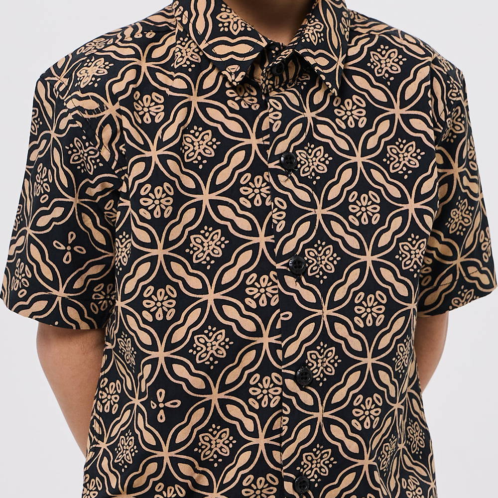 Black shirt with beige floral pattern worn by a person on a white background