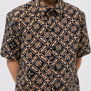 Black shirt with beige floral pattern worn by a person on a white background