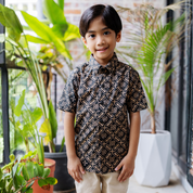 Child wearing a patterned shirt standing among potted plants