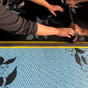 Two people measuring fabric with a yellow ruler on a floral-patterned surface.