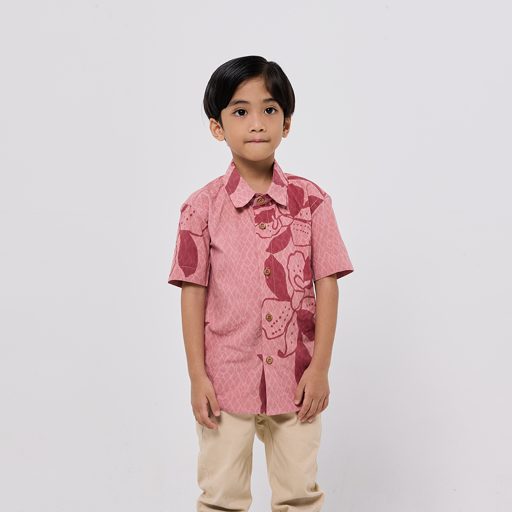 Child wearing a pink patterned shirt and beige pants on a white background