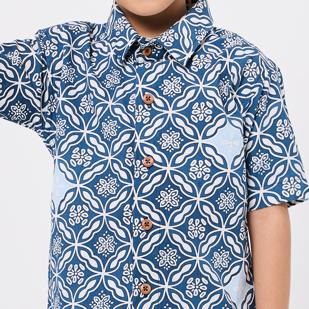 Person wearing a blue and white patterned shirt with buttons on a light gray background