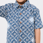 Person wearing a blue and white patterned shirt with buttons on a light gray background