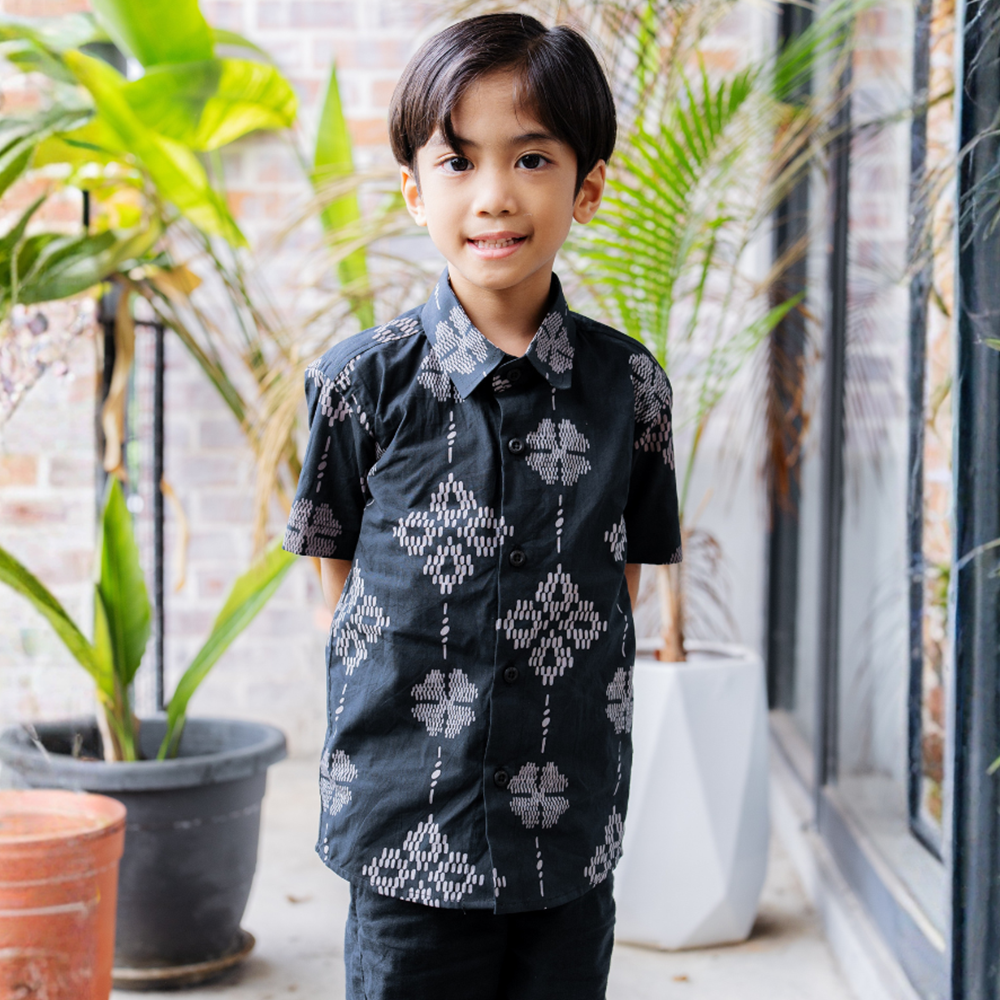 Child wearing a black patterned shirt standing in front of plants
