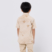 Child wearing a beige patterned shirt and pants on a white background
